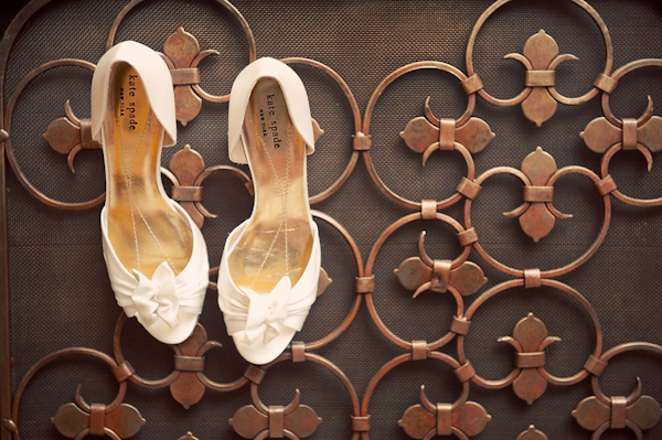 a pair of white wedding shoes with ribbons hanging from copper fireplace screen - photo by Houston based wedding photographer Adam Nyholt